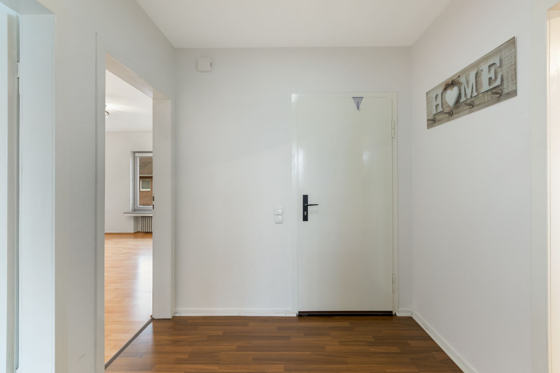 Heller Flur mit weißer Tür, Holzfußboden und Wanddeko mit Schriftzug HOME.
