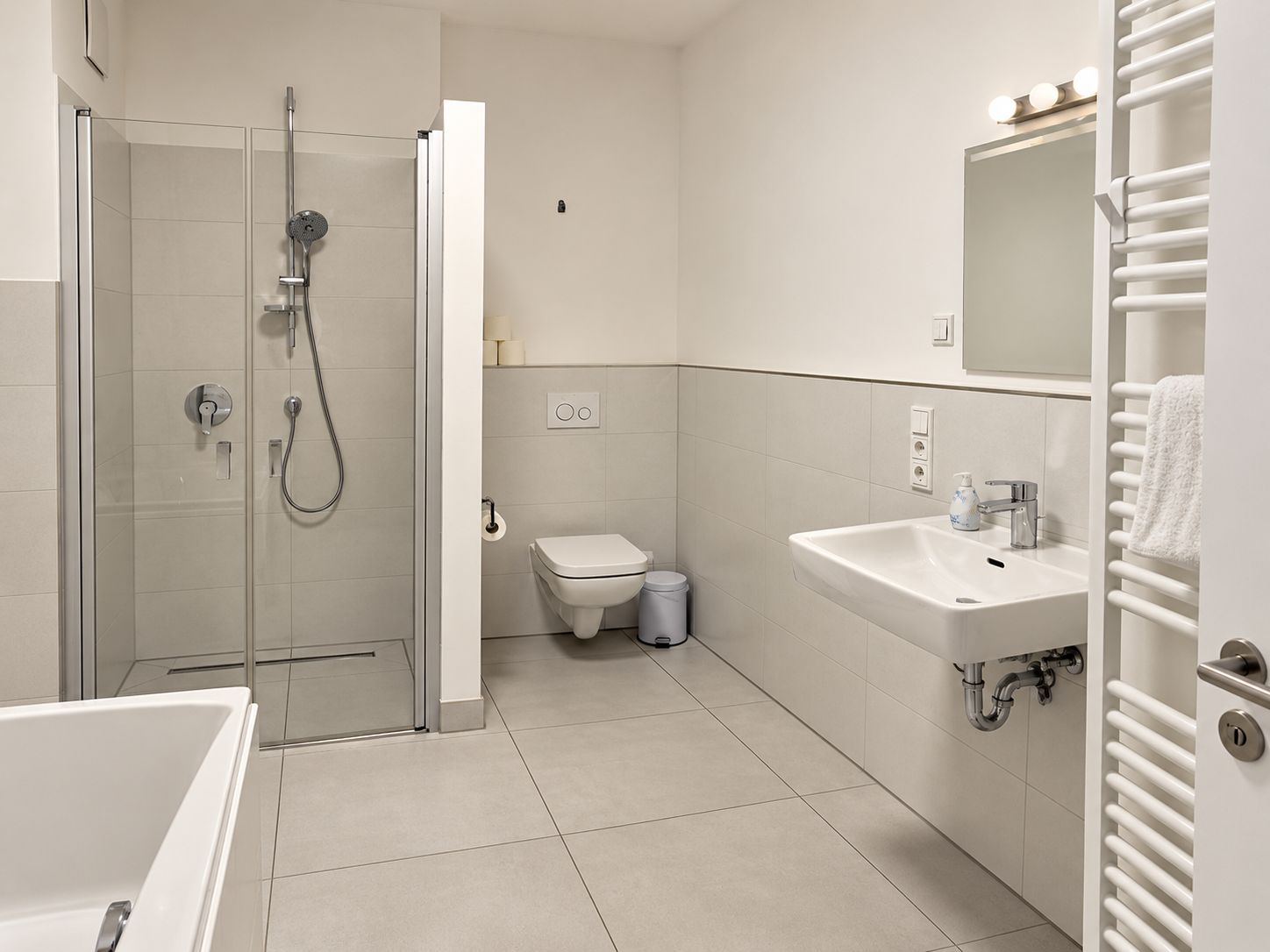 Modernes Bad mit Dusche, Badewanne, Wand-WC, Waschbecken und Handtuchheizkörper.