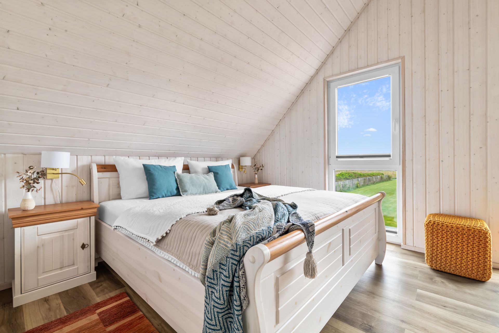 Helles Schlafzimmer mit Doppelbett, Holzmöbeln und großem Fenster mit Blick ins Grüne.