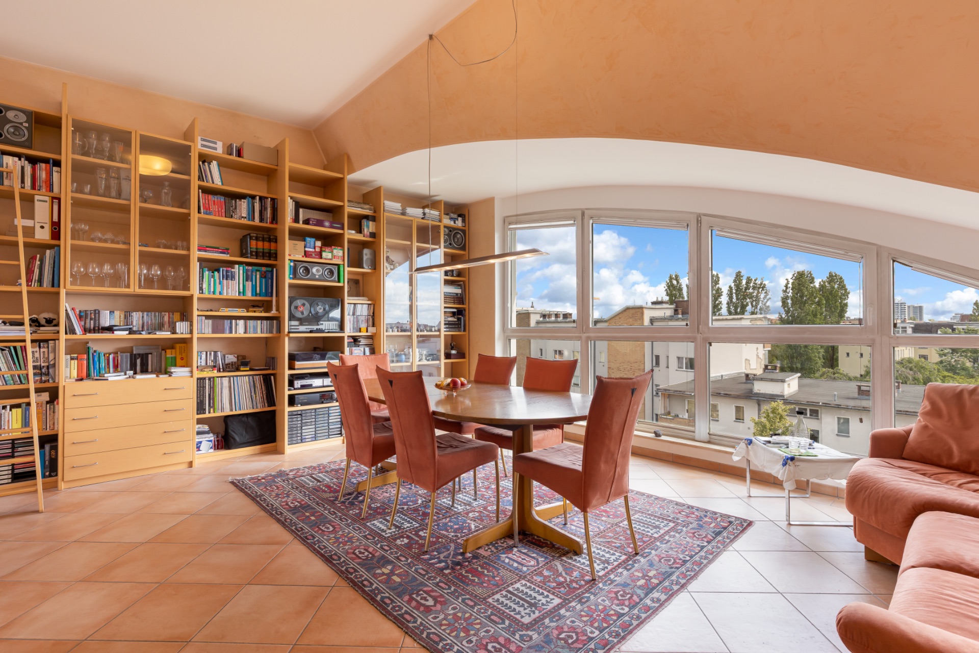 Heller Essbereich mit Holztisch, sechs Stühlen, Bücherregalen und großen Fenstern mit Stadtblick.