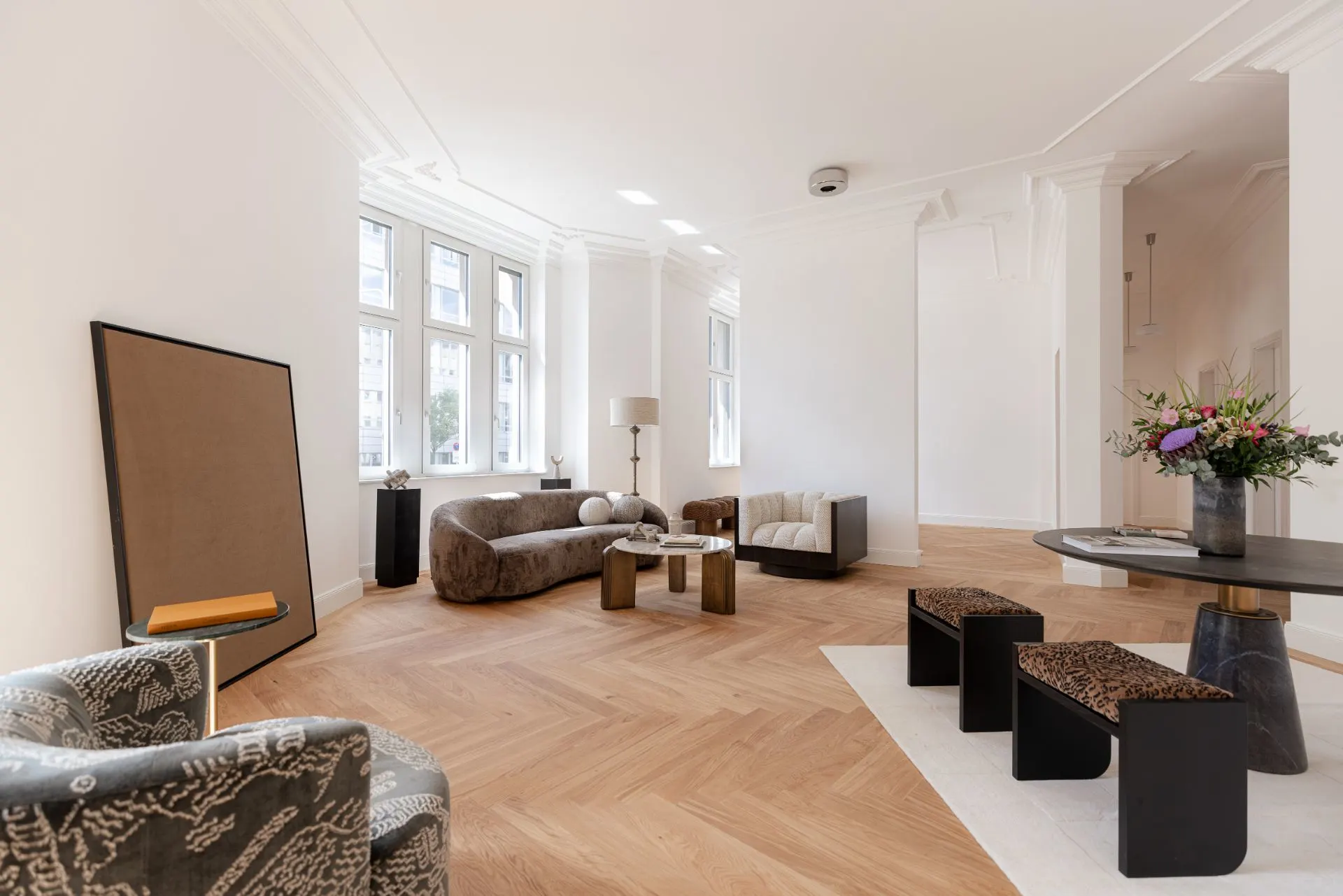 Helles Wohnzimmer mit Sofas, Sesseln, Couchtischen, einem runden Tisch und drei Hockern auf Holzfußboden.