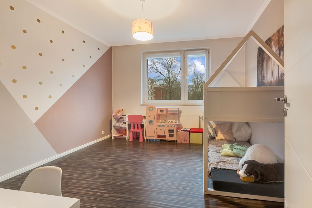 Modernes Kinderzimmer mit Spielküche, Spielzeug und einem Hausbett bei Tageslicht.
