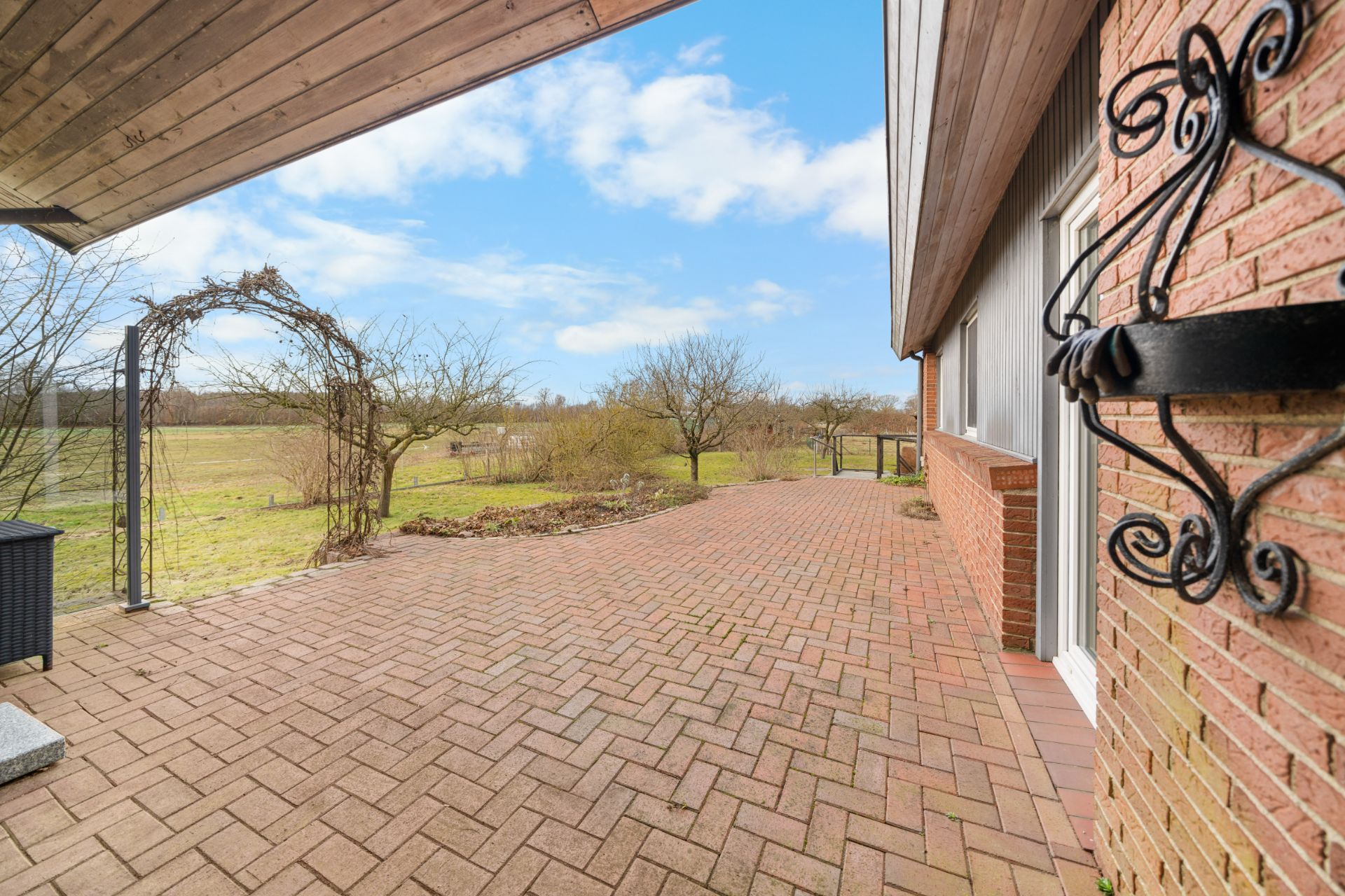Gepflasterte Terrasse an einem Haus mit Blick auf einen Garten und Wiese.