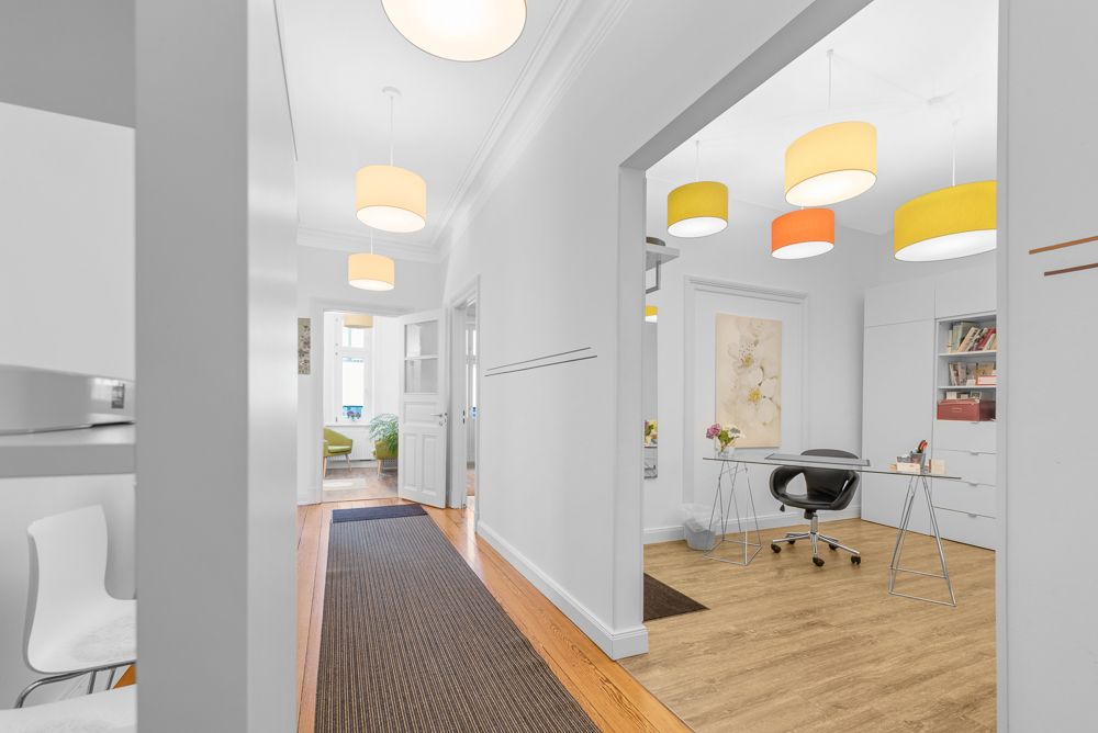Heller Flur mit Holzboden, angrenzendem Arbeitszimmer und bunten Deckenlampen.