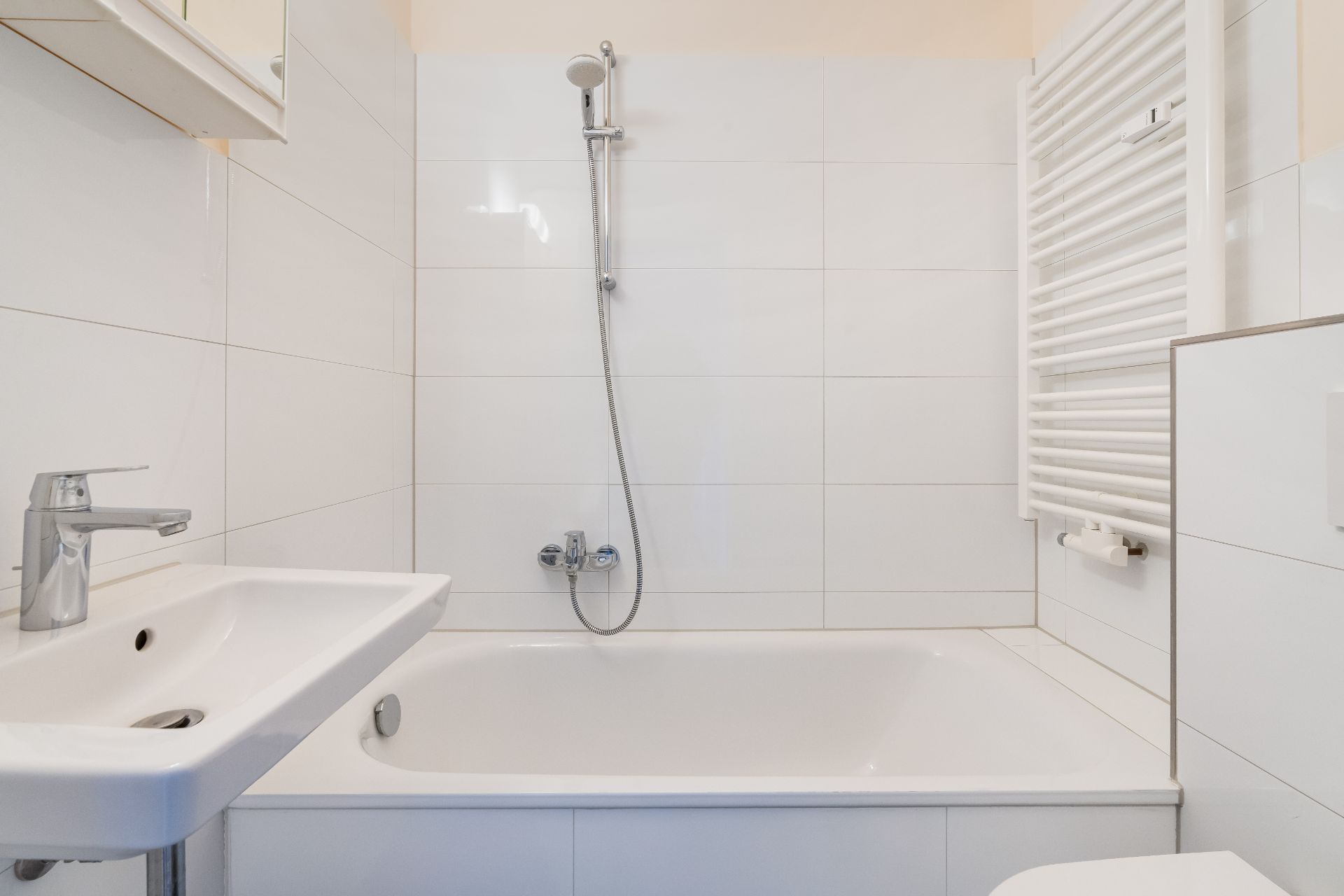 Modernes Badezimmer mit Badewanne, Duscharmatur, Waschbecken und Handtuchheizkörper.
