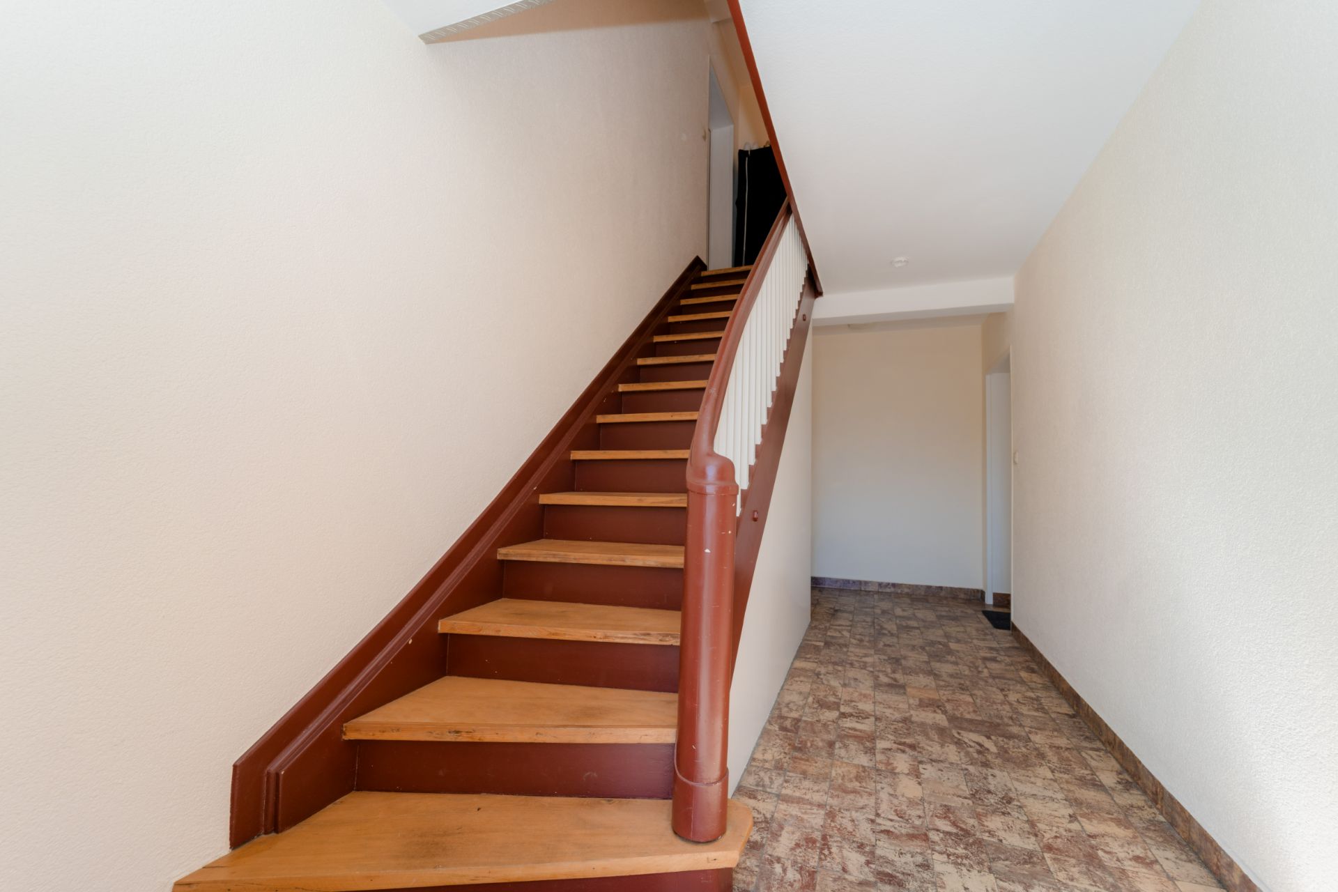 Flur mit brauner Holztreppe und gefliestem Boden in einem Wohnhaus.