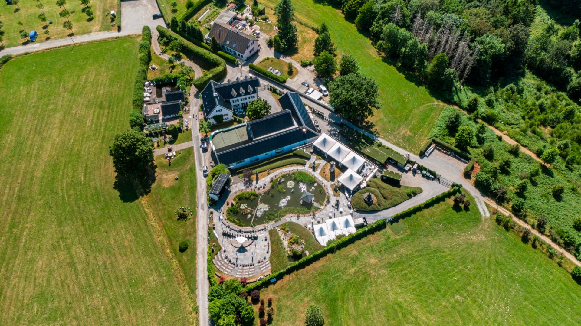Luftaufnahme eines großen Wohnanwesens mit Garten, Teich und umliegenden Wiesen.