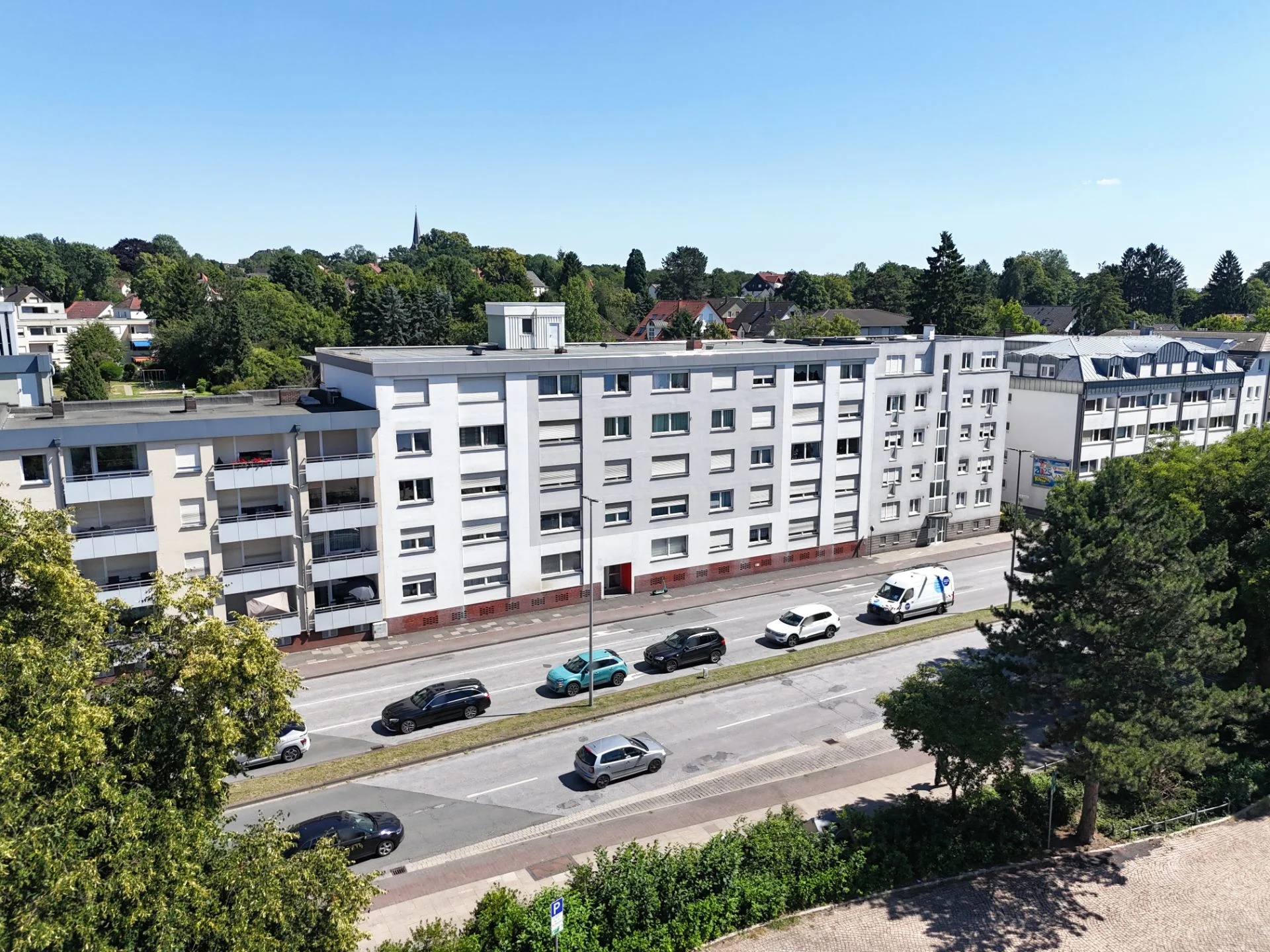 Mehrstöckiges Wohngebäude an einer Straße mit parkenden Autos, Bäume im Vordergrund.