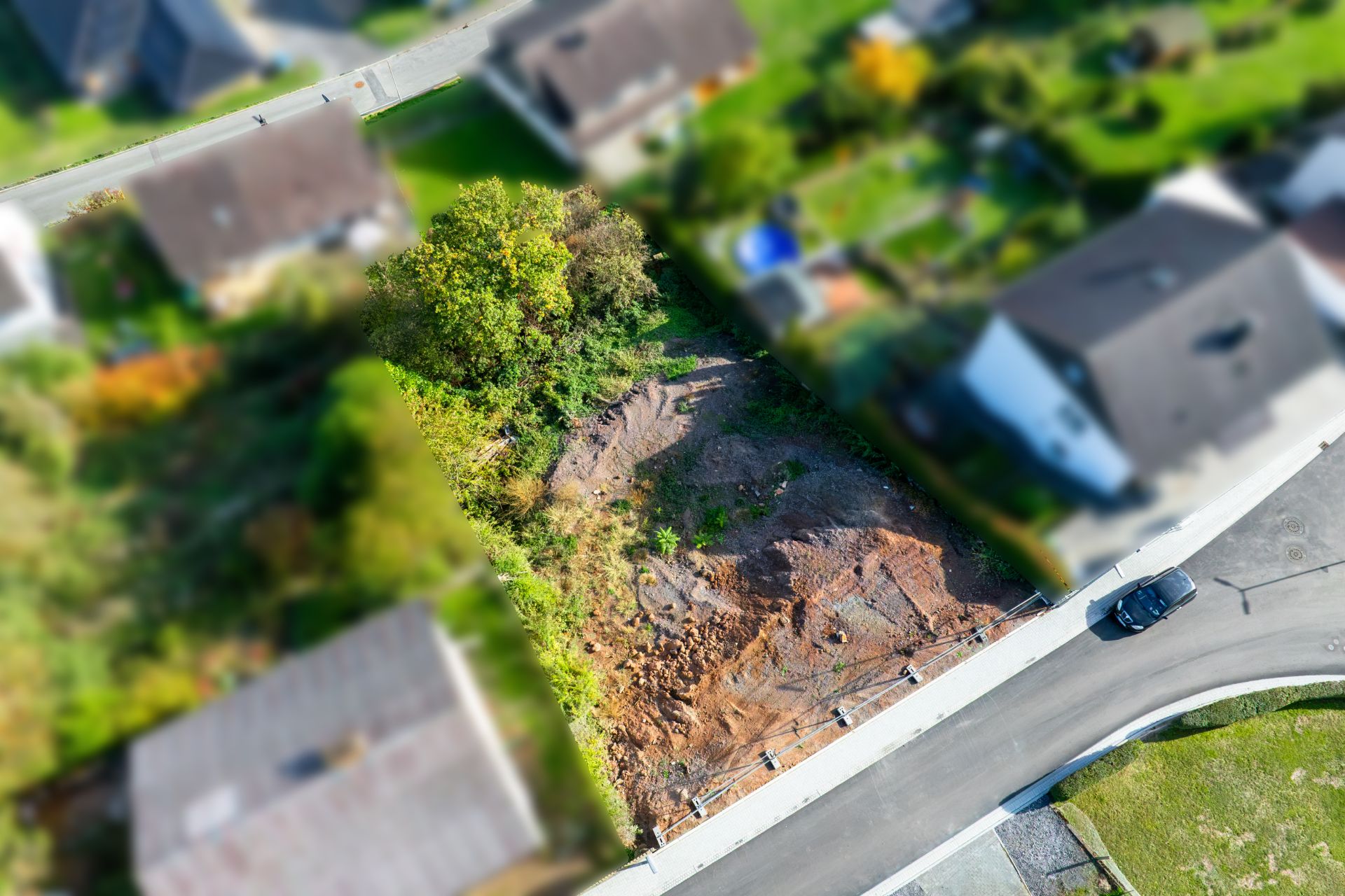 Luftaufnahme eines unbebauten Grundstücks inmitten von Wohnhäusern an einer Straße.