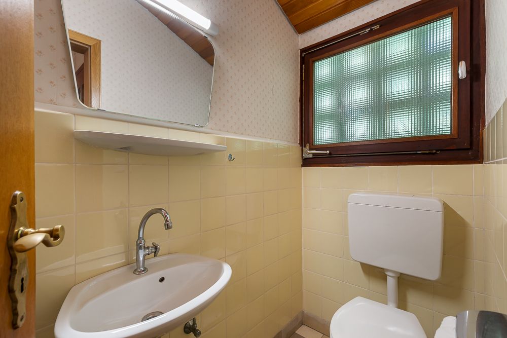 Kleines Badezimmer mit Waschbecken, Spiegel, WC und Fenster mit Milchglas.