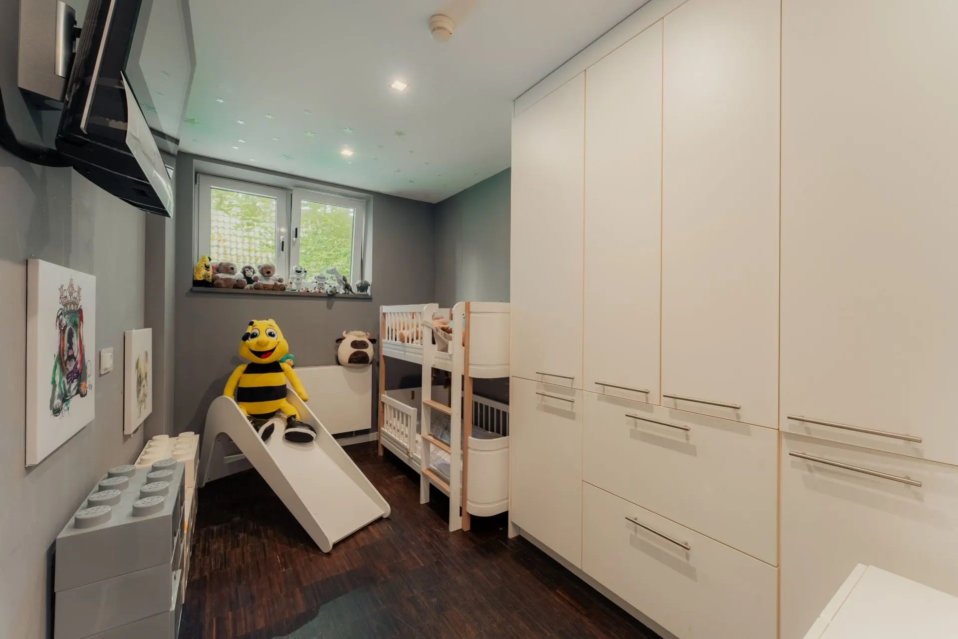 Kinderzimmer mit Etagenbett, Rutsche, Kuscheltieren und weißen Schränken.