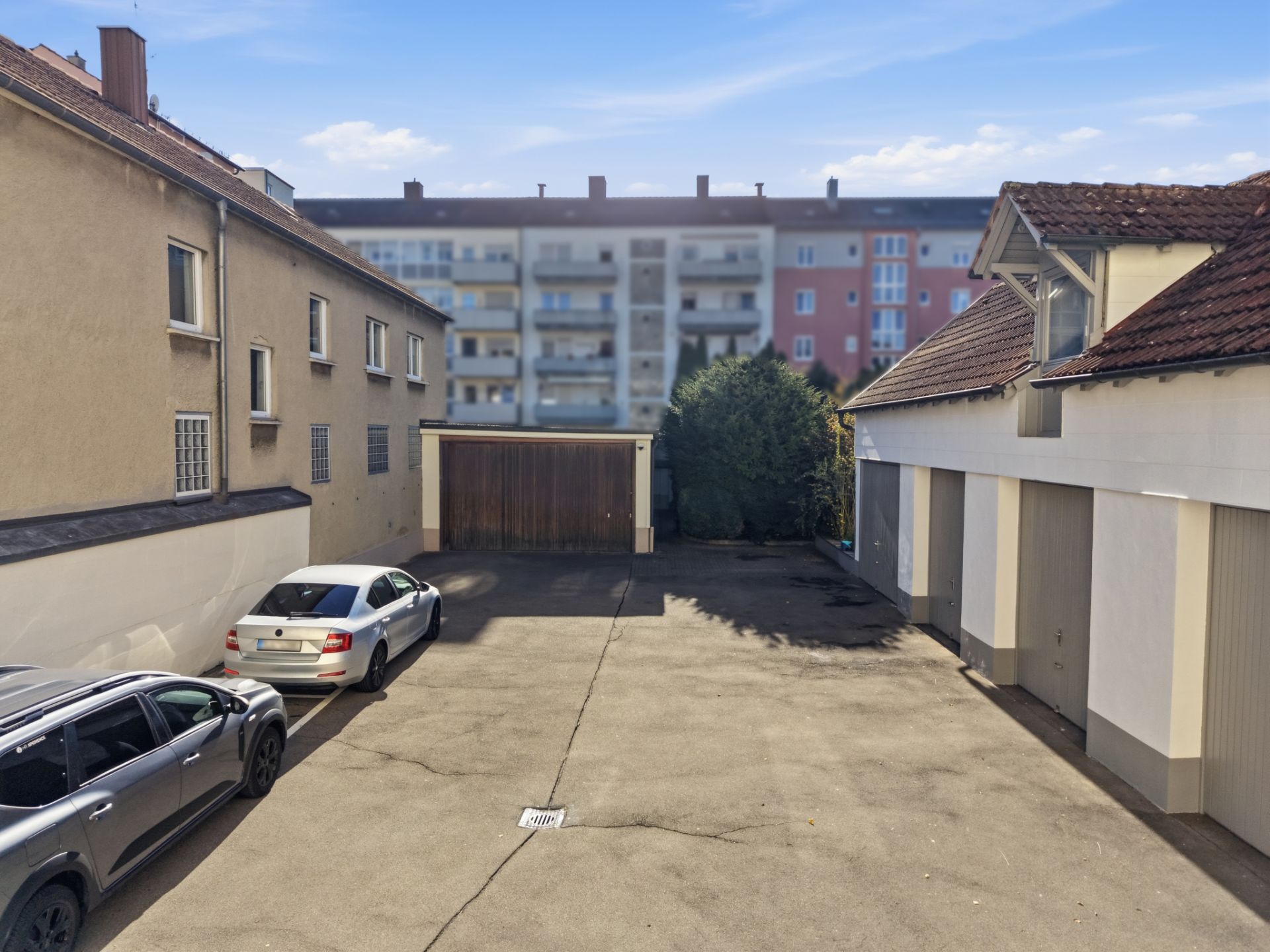 Asphaltierter Innenhof mit geparkten Autos, Garagen und Wohngebäuden im Hintergrund.