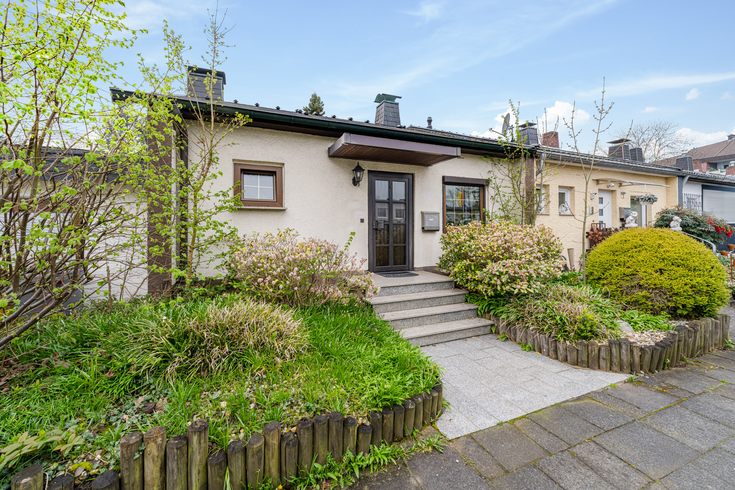 Eingang eines Einfamilienhauses mit Treppe, Garten und Sträuchern vor der Tür.
