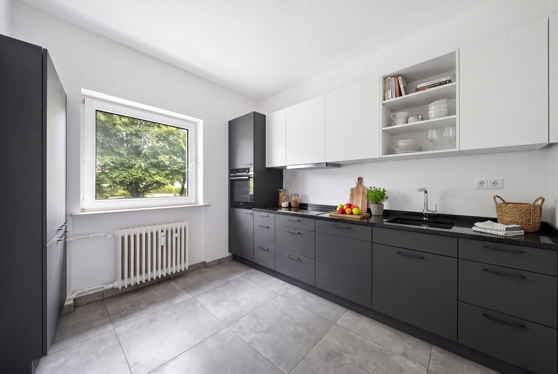 Moderne Küche mit grauen Unterschränken, weißen Oberschränken und großem Fenster mit Blick ins Grüne.