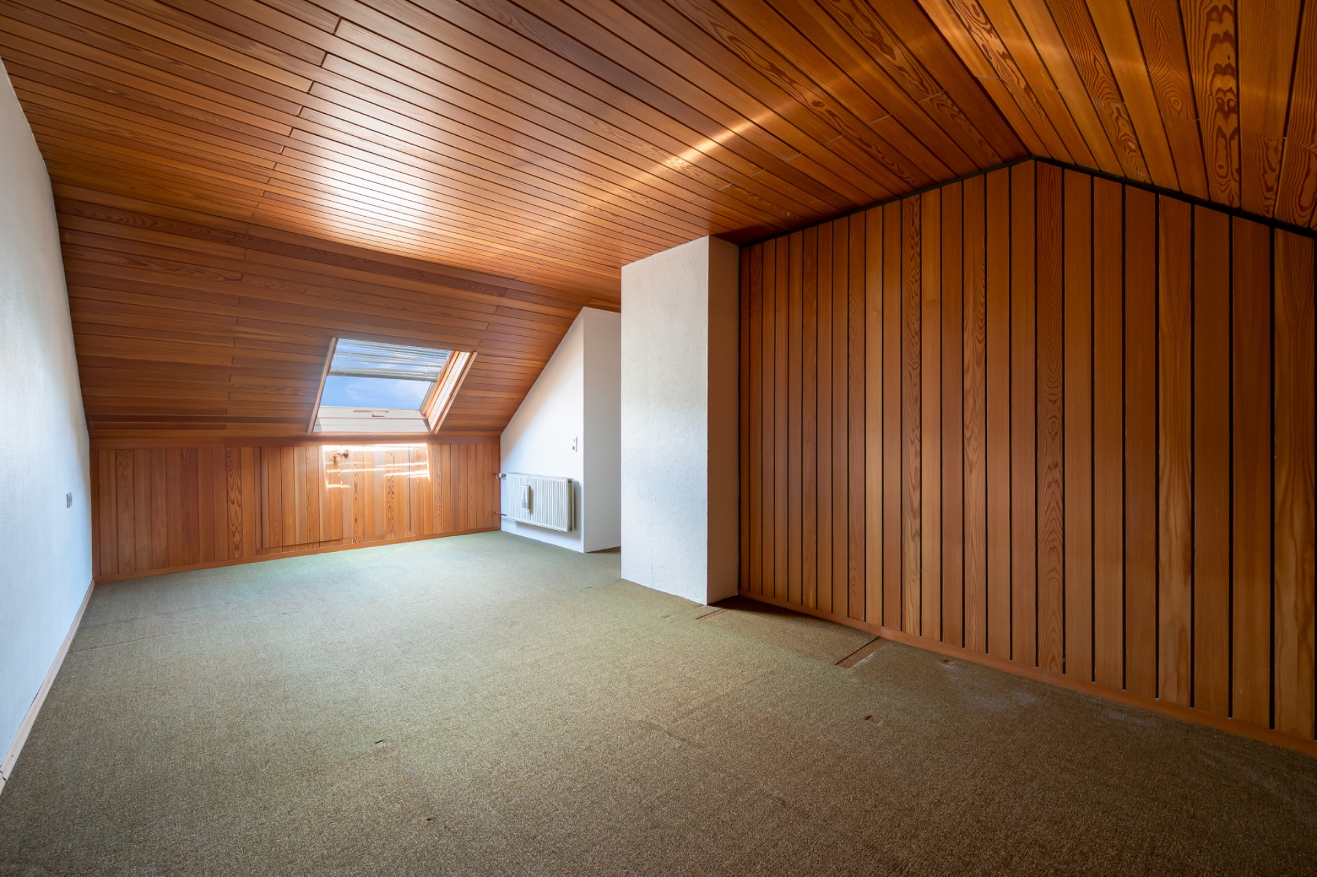 Leerer Dachraum mit Holzverkleidung, schräger Decke und großem Dachfenster.