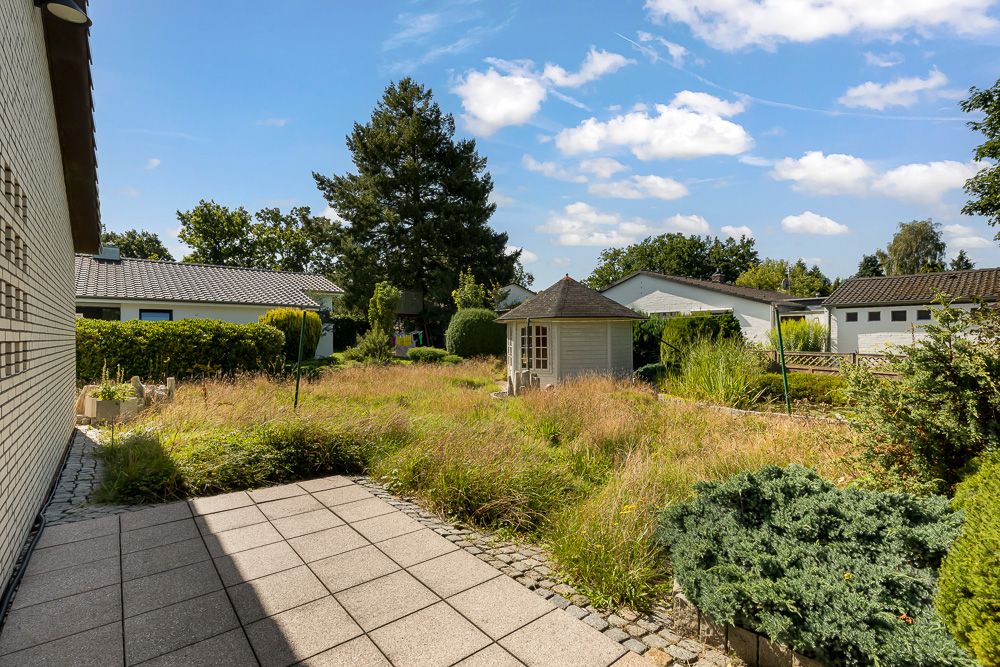 Garten mit Terrasse, Rasenfläche, Sträuchern und einem kleinen Pavillon bei Tageslicht.