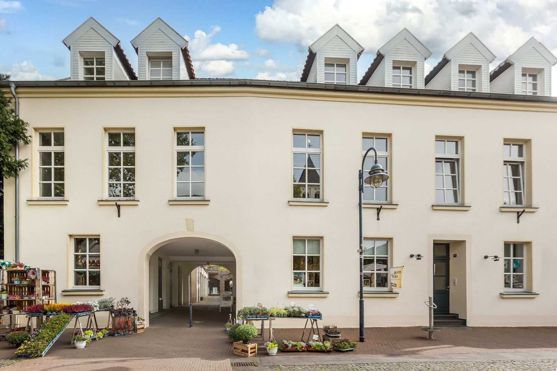 Helles Wohnhaus mit weißen Fenstern, Blumenkästen und überdachtem Durchgang im Erdgeschoss.