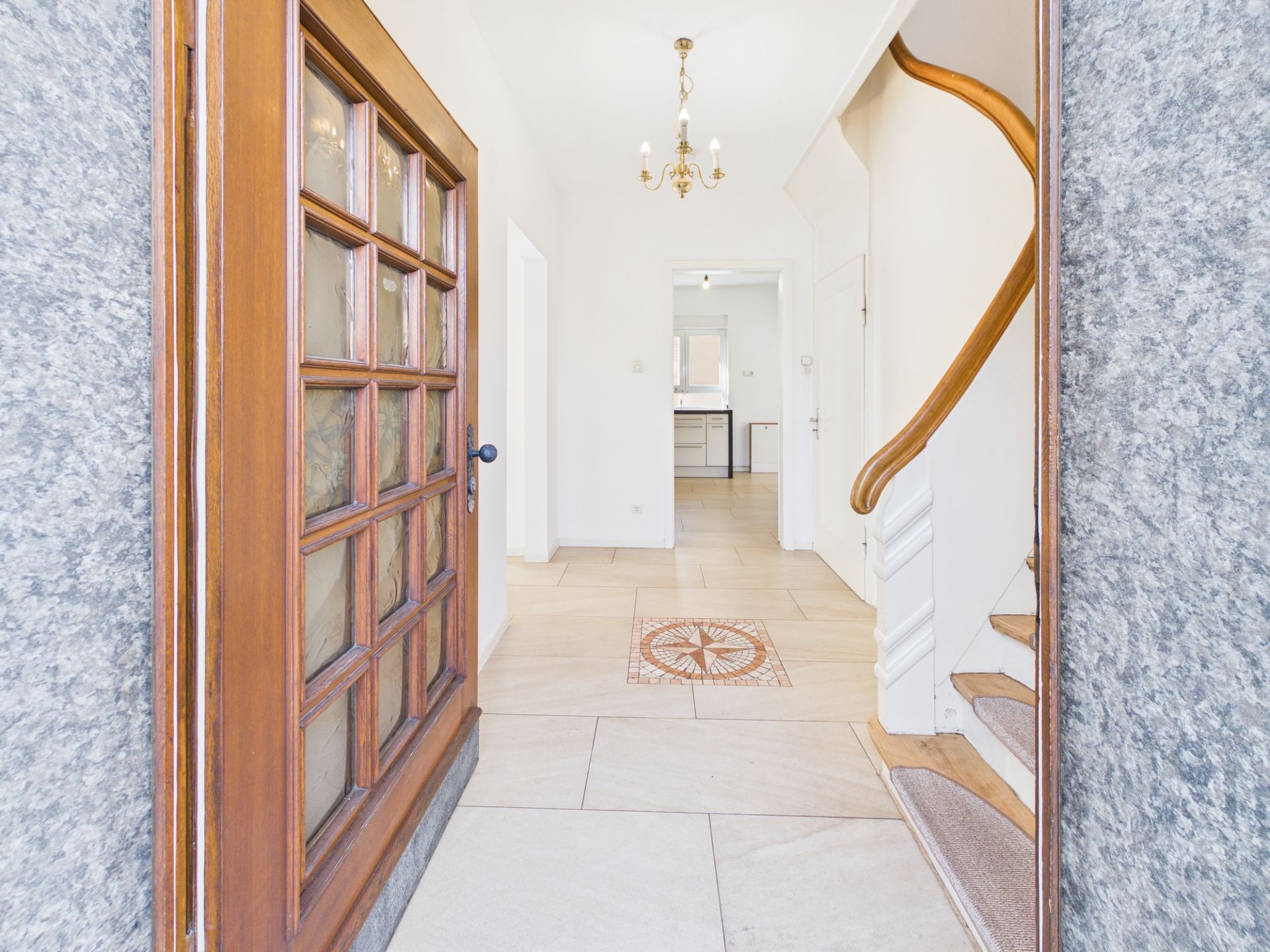 Offene Haustür mit Blick auf einen Flur, Treppe rechts und Küche im Hintergrund.
