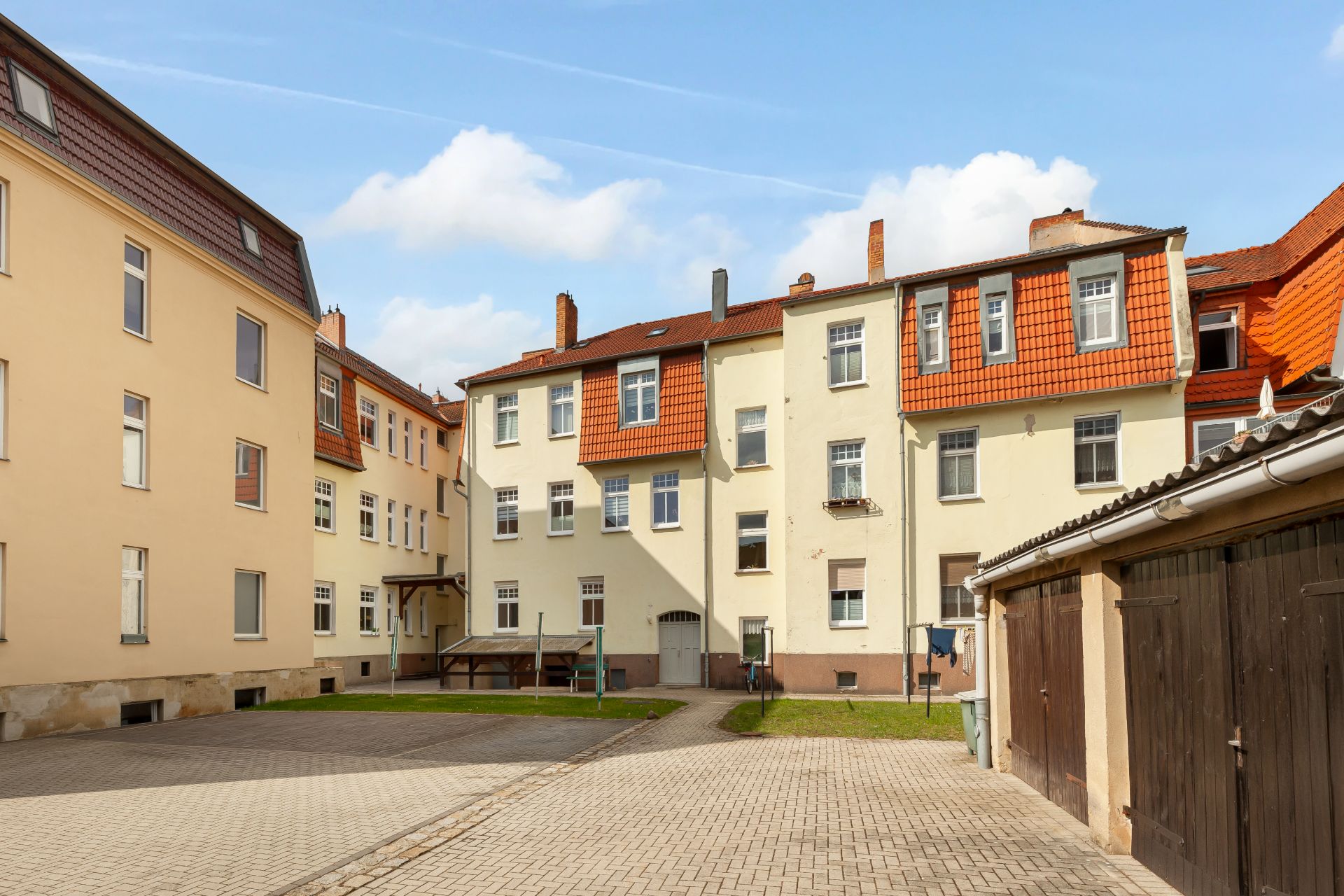Hof eines Mehrfamilienhauses mit Garagen und Pflastersteinen bei Tageslicht.