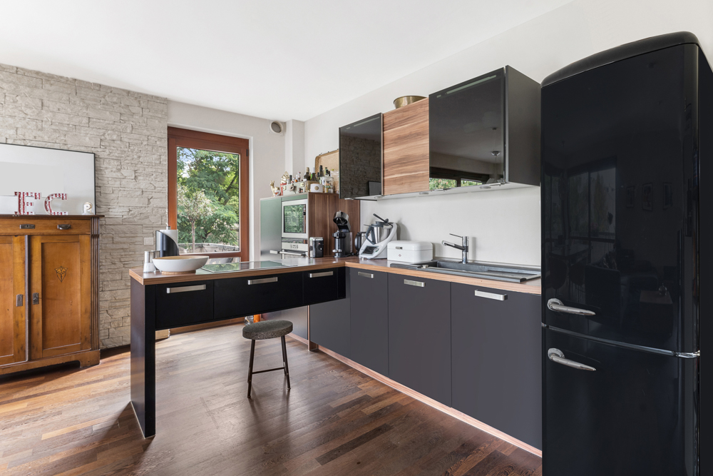 Moderne Küche mit schwarzen Schränken, Holzarbeitsplatte und großem schwarzen Kühlschrank.