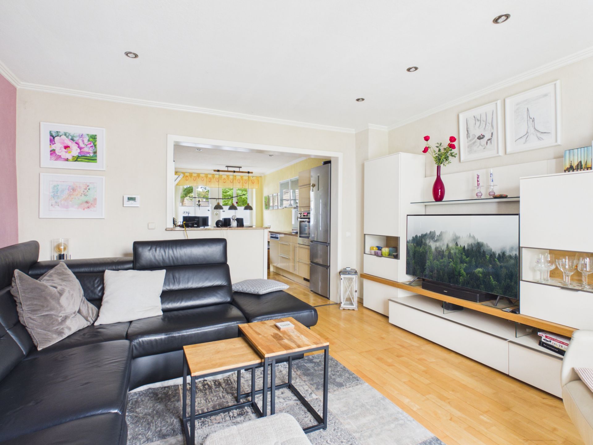 Modernes Wohnzimmer mit schwarzem Sofa, Couchtisch, TV und Blick in offene Küche.