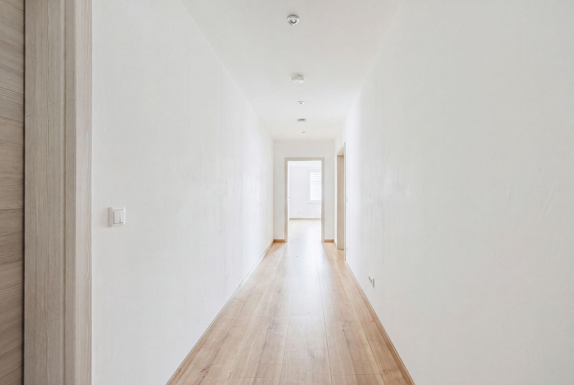 Heller Flur mit Holzfußboden und weißen Wänden in einer Wohnung.