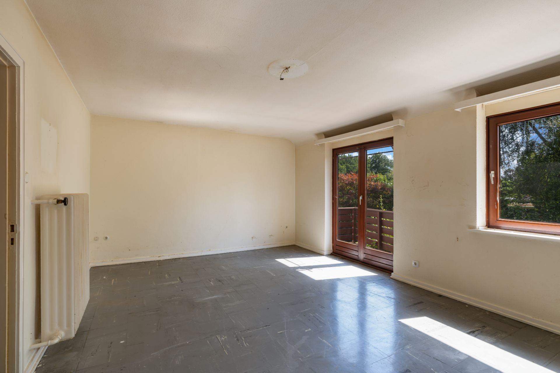 Leeres Zimmer mit grauem Boden, großem Fenster und Glastür zu einem Balkon.
