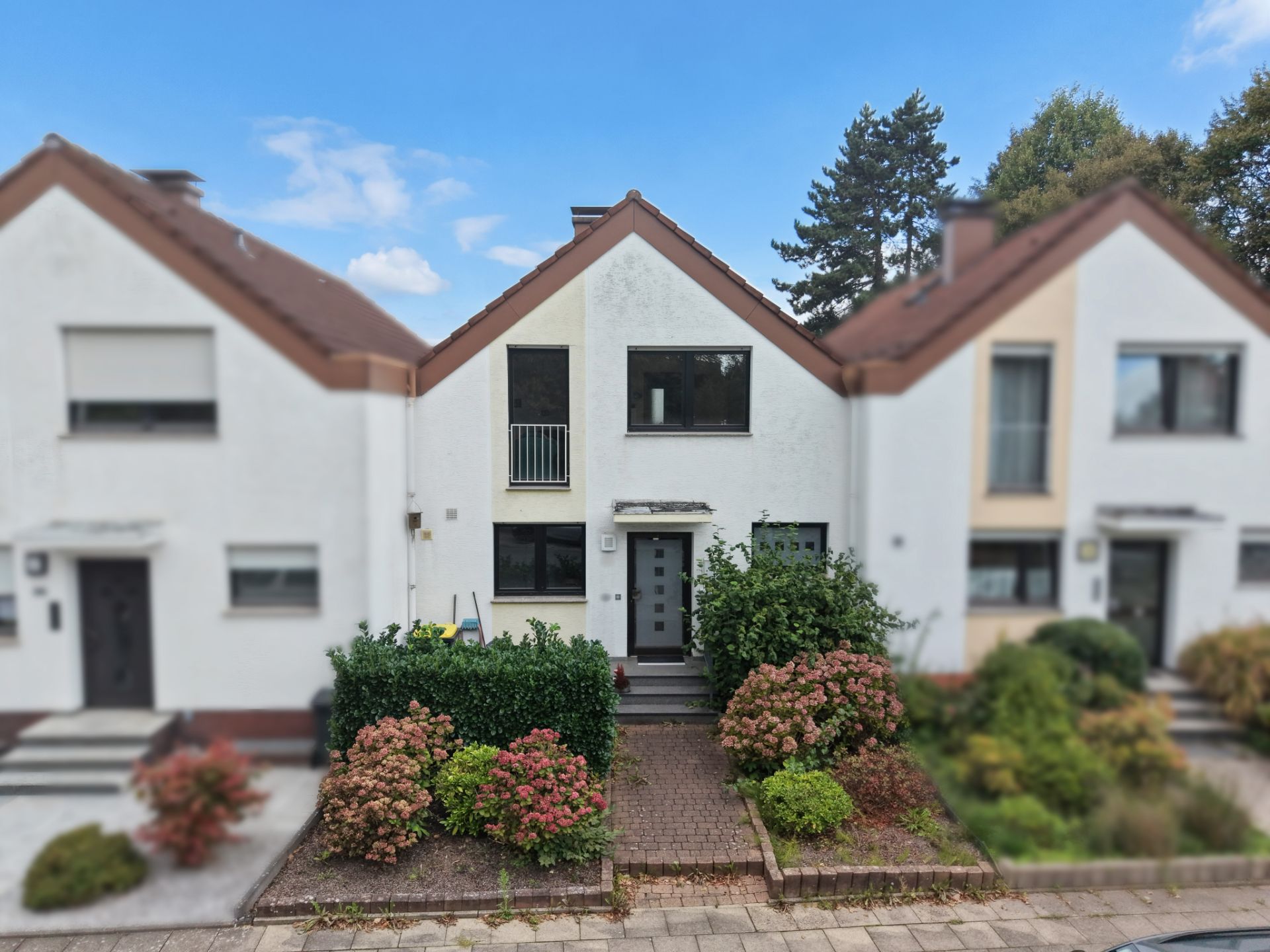 Reihenhaus mit weißer Fassade, Vorgarten und umgeben von weiteren Häusern.