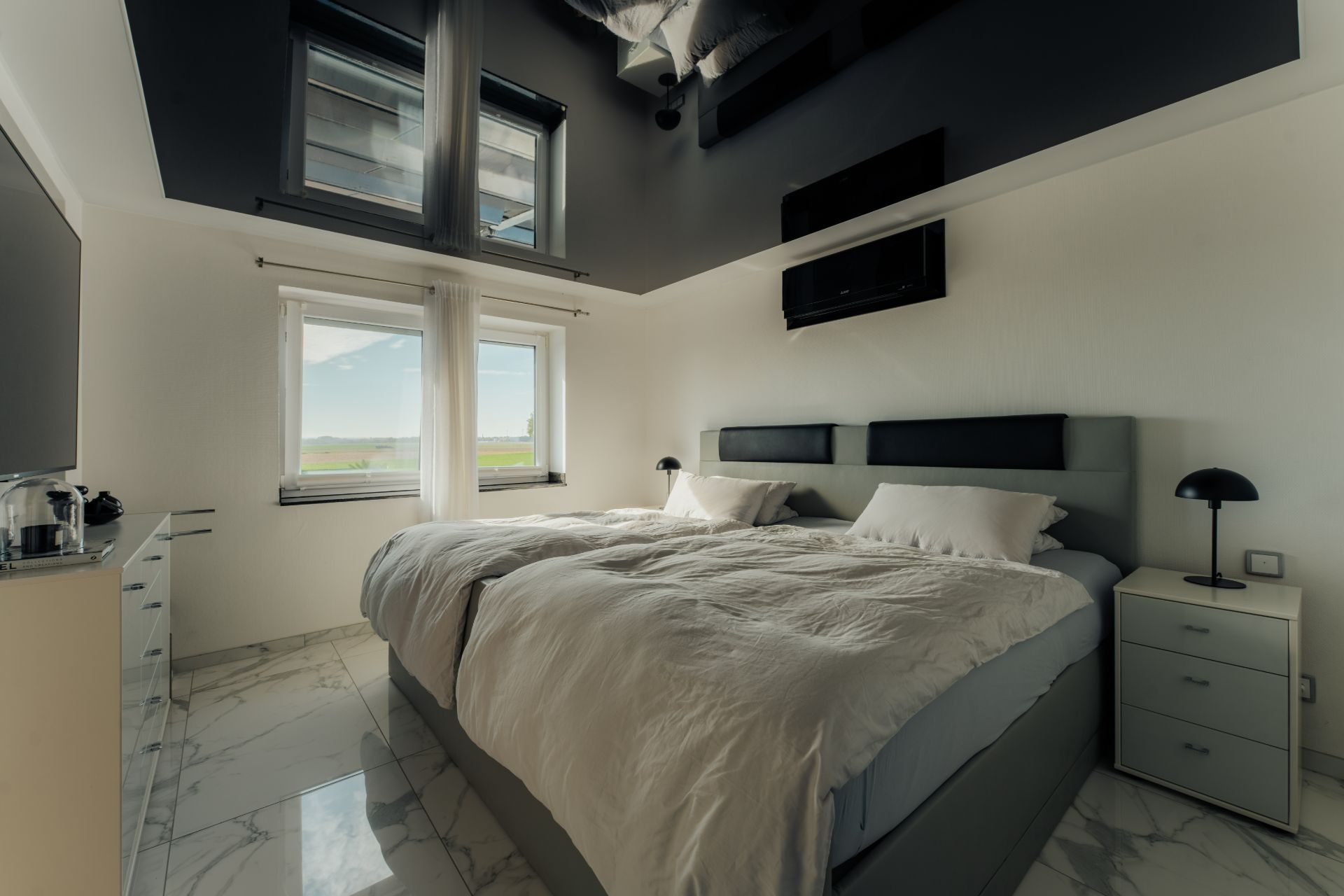 Modernes Schlafzimmer mit großem Bett, zwei Fenstern, Nachttischen und Marmorfußboden.