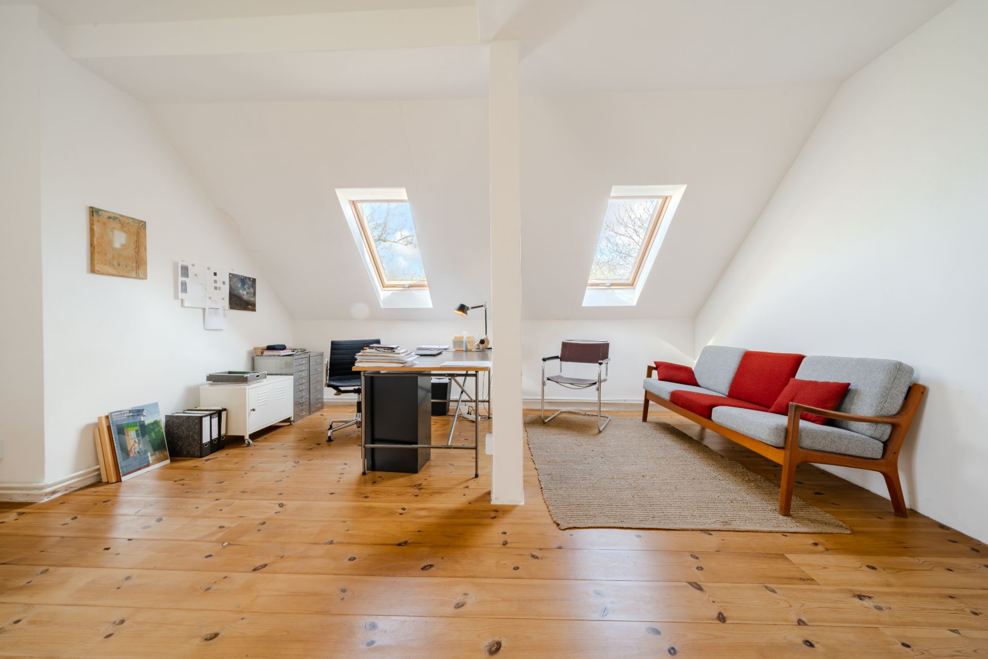 Helles Dachgeschosszimmer mit Schreibtisch, Sofa, Stuhl und schrägen Fenstern auf Holzboden.