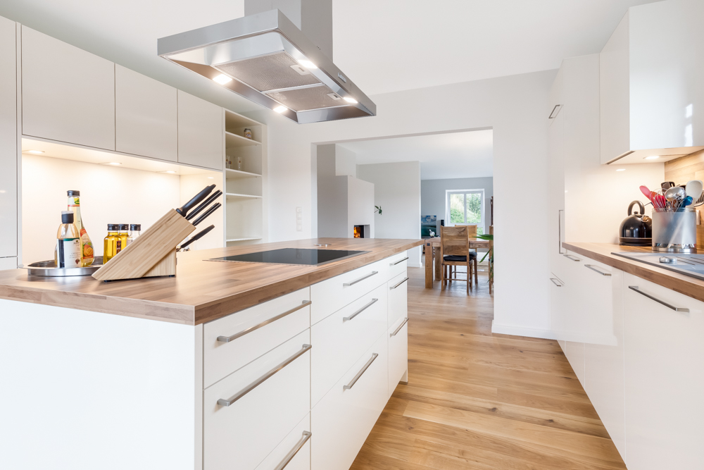 Moderne Küche mit Kochinsel, weißen Schränken und Holzarbeitsplatten, Blick auf Esszimmer.