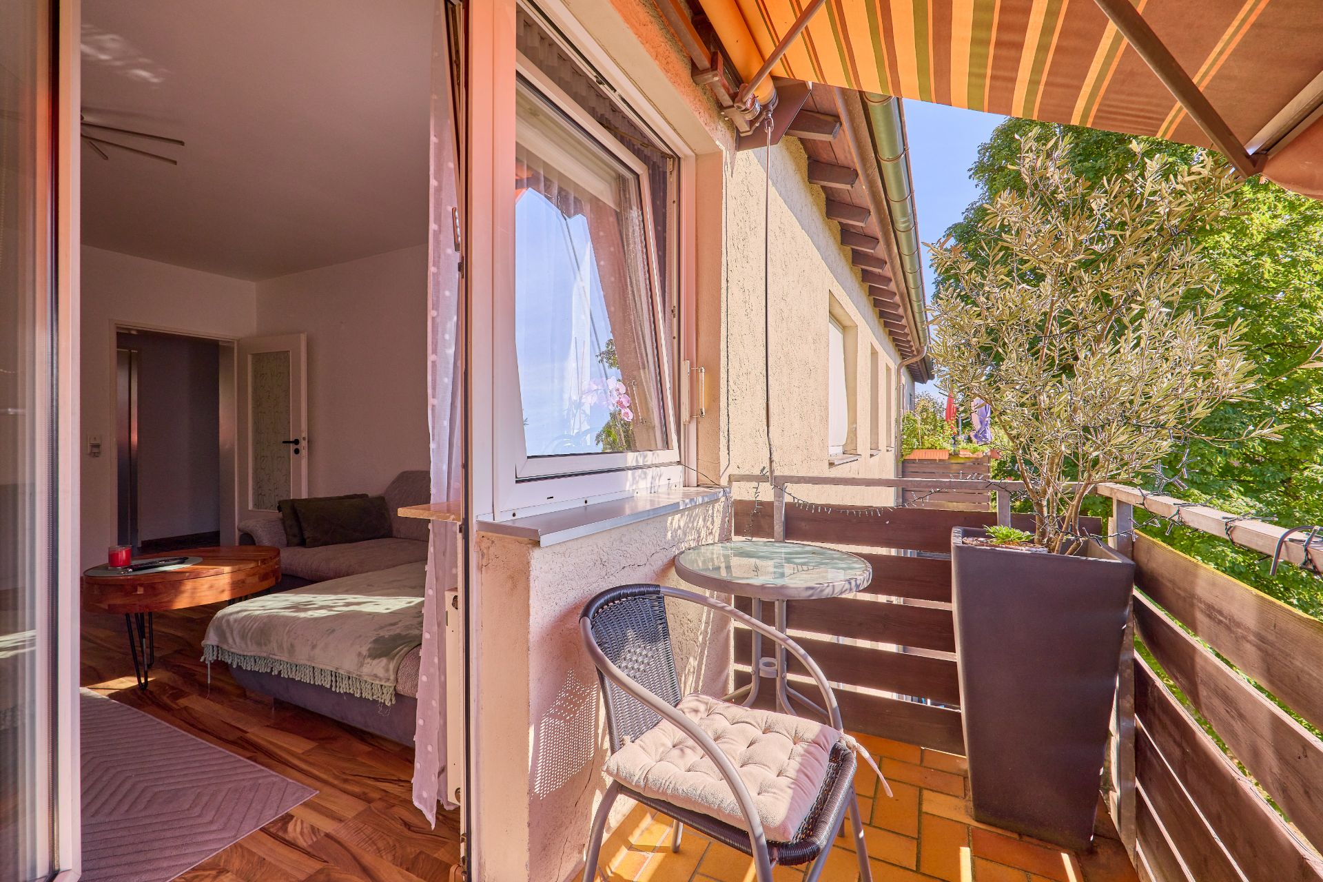 Kleiner Balkon mit Tisch, Stuhl, Pflanze und Markise, Blick ins helle Wohnzimmer.