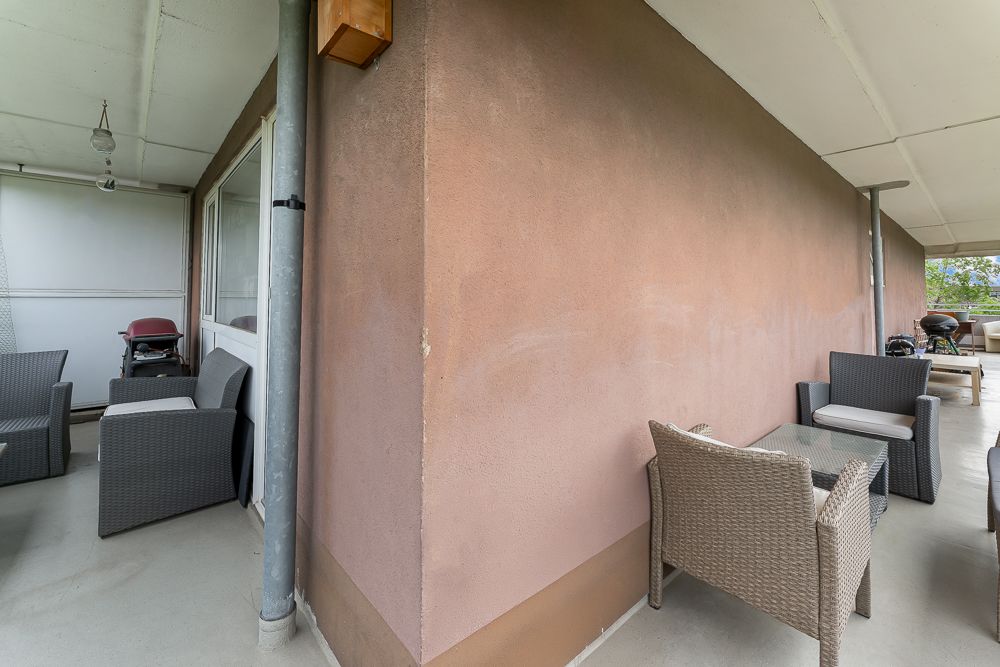 Überdachte Terrasse mit mehreren Sitzgruppen aus Rattan und einem Grill.