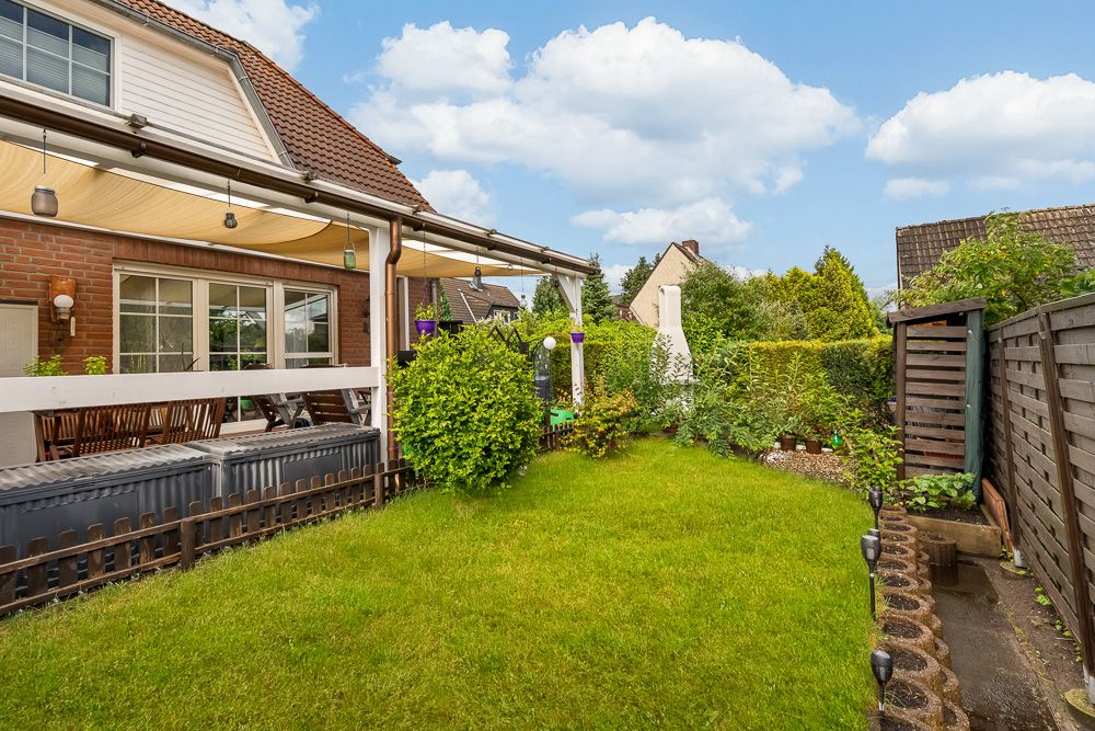 Grüner Garten mit Terrasse, Holzzaun und überdachtem Sitzbereich an einem Wohnhaus.