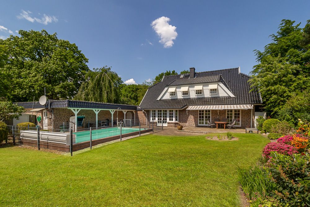 Backsteinwohnhaus mit großem Garten und überdachtem Pool, umgeben von Bäumen und Blumen.