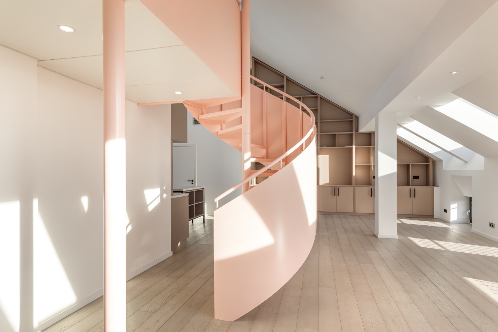 Heller Raum mit rosa Wendeltreppe und Einbauschränken unter einer Schräge.