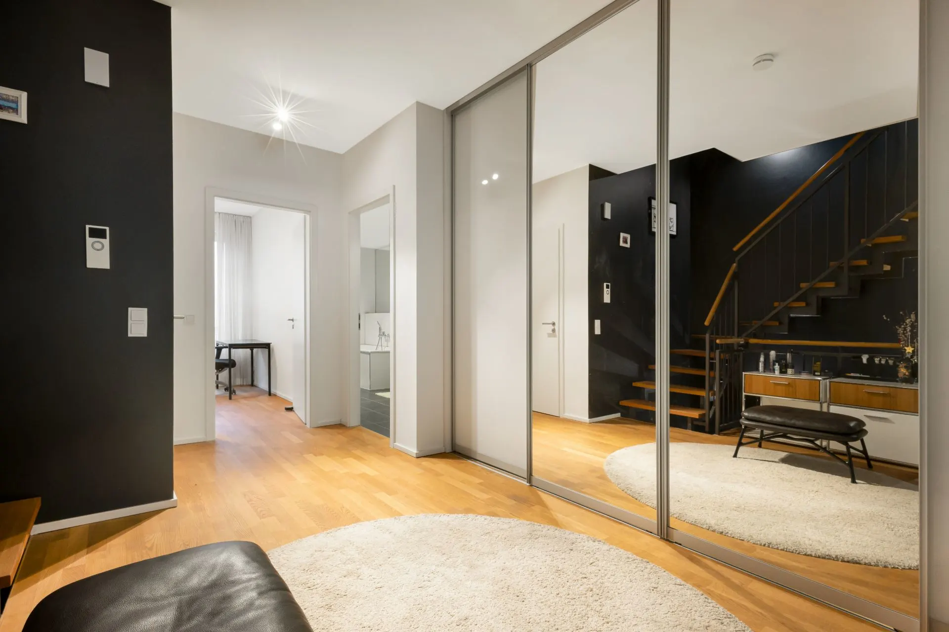 Moderner Flur mit Holzfußboden, Spiegelschränken, Teppich und Treppe im Hintergrund.