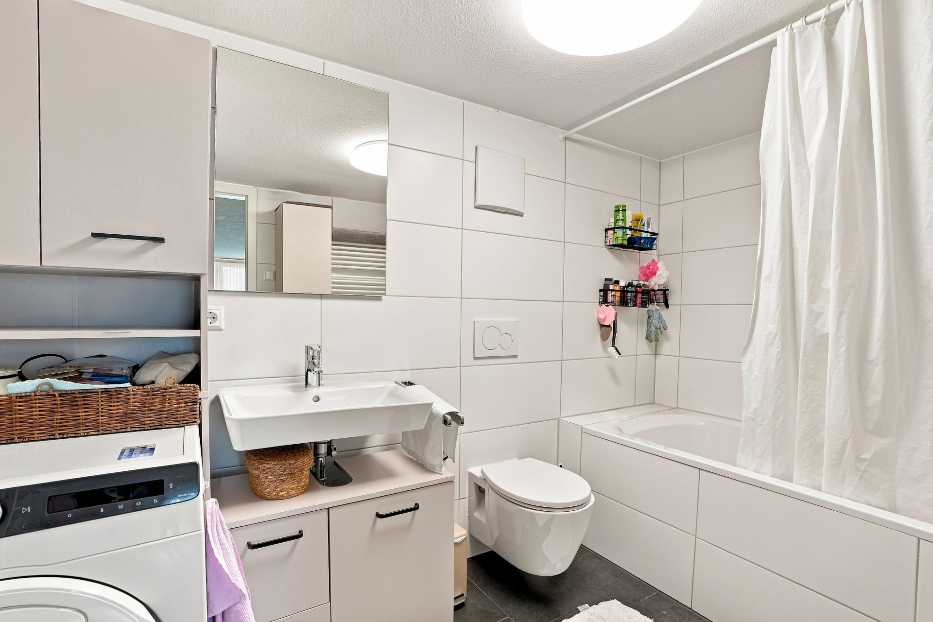 Modernes Badezimmer mit Waschmaschine, Waschbecken, Toilette und Badewanne mit Duschvorhang.