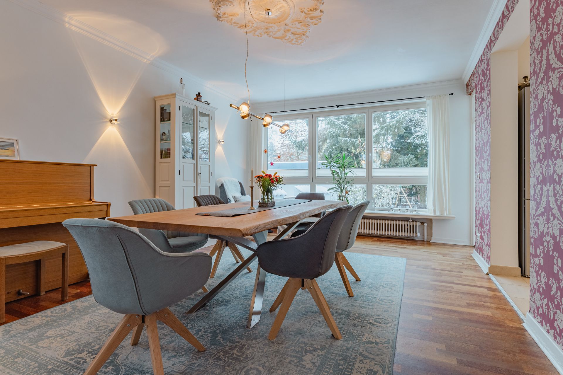 Helles Esszimmer mit Holztisch, sechs Stühlen, Klavier, großem Fenster und Pflanze.
