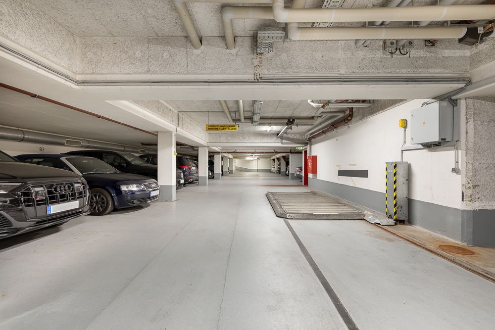 Tiefgaragenbereich mit parkenden Autos und sichtbaren Rohrleitungen an der Decke.