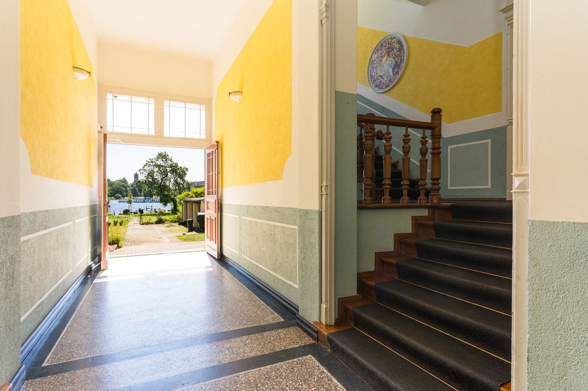 Heller Flur mit offenen Türen, Treppe rechts und Blick auf Garten mit Bäumen.