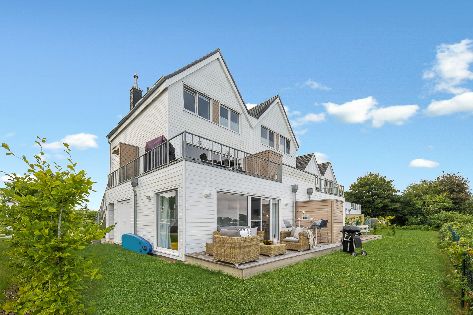 Modernes, weißes Wohnhaus mit Terrasse und Garten, Gartenmöbeln und Grill.