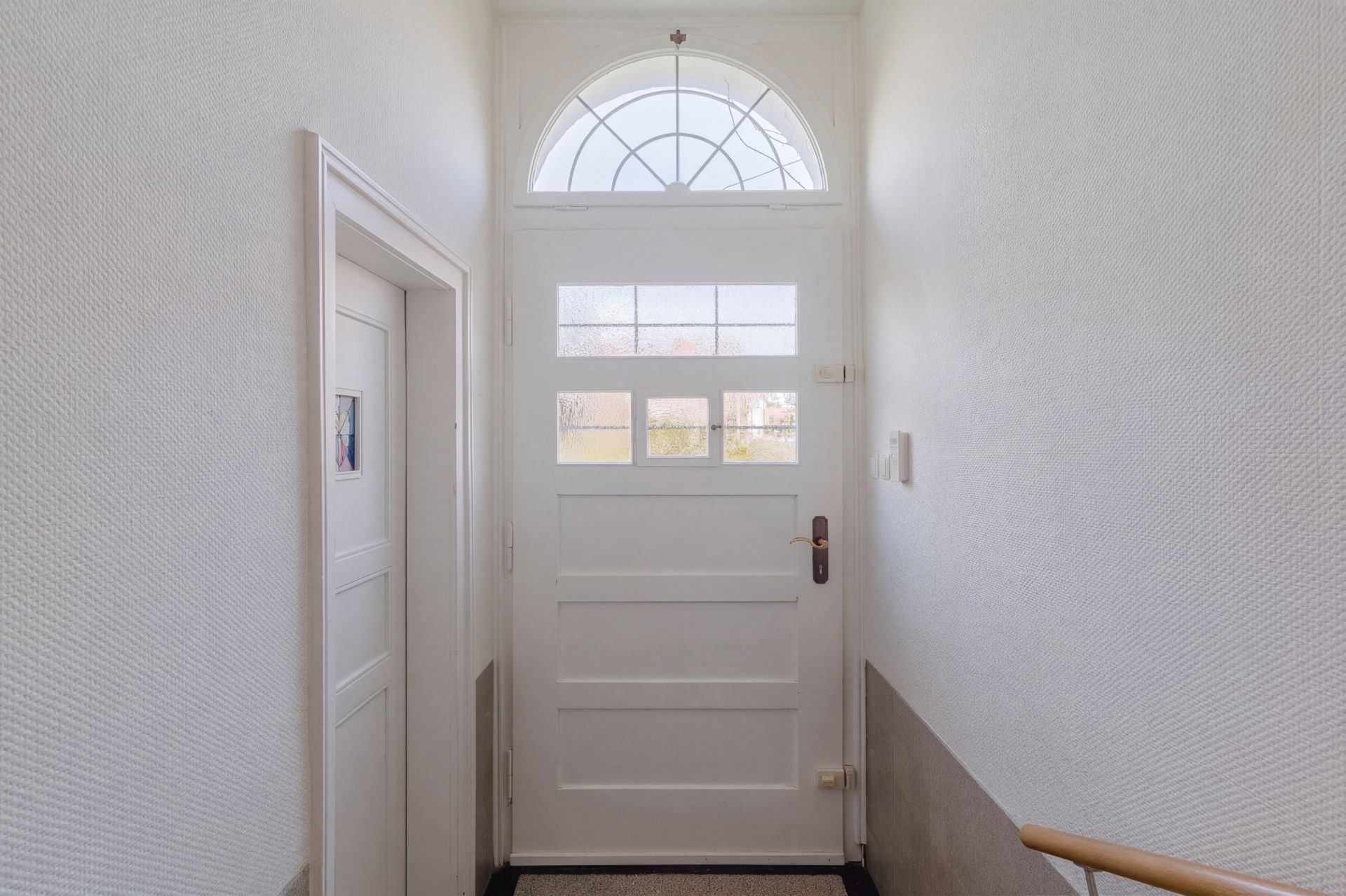 Heller Flur mit weißer Haustür und kleinem Fenster über der Tür.