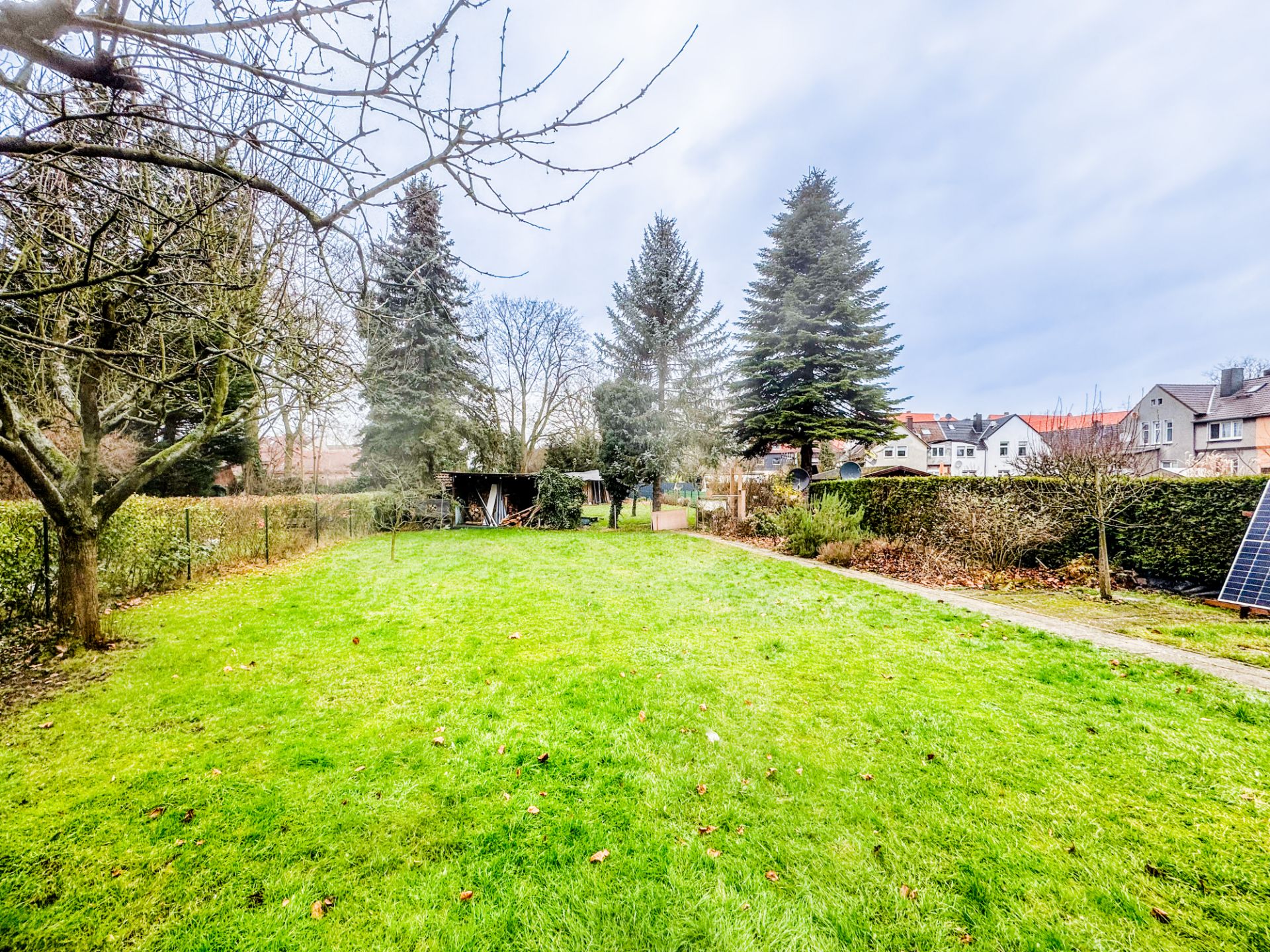 Großer Garten mit Rasen, Bäumen und Schuppen, daneben einige Wohnhäuser.