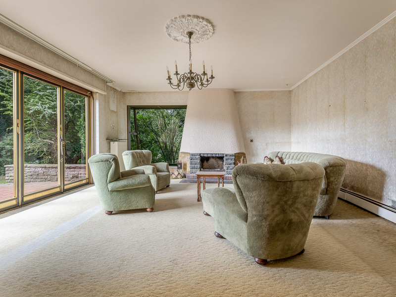 Wohnzimmer mit grünem Sofa, Sesseln, Kamin, Kronleuchter und großen Fenstern zum Garten.