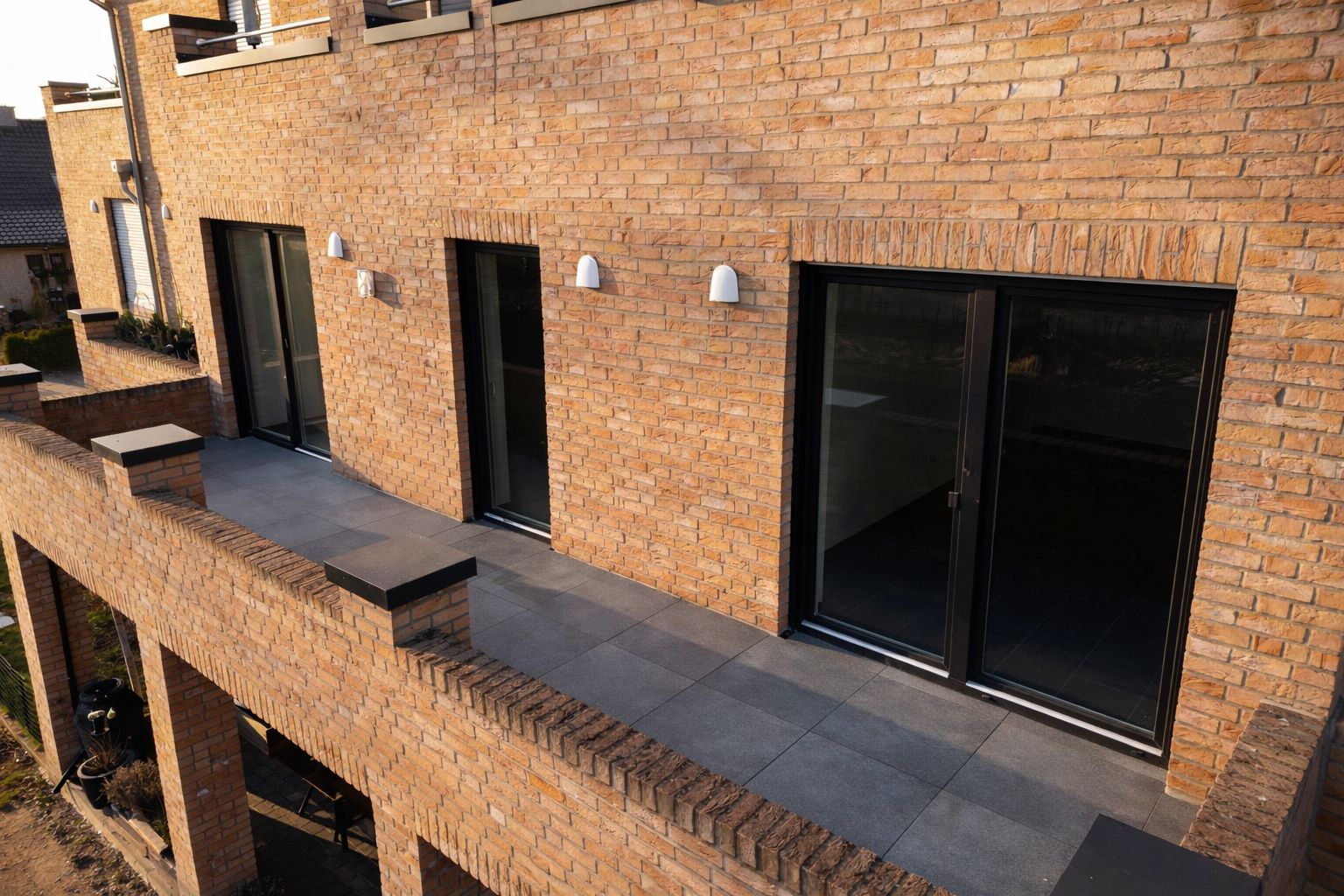 Moderner Balkon mit Fliesenboden und mehreren Glastüren an einer Backsteinwand.