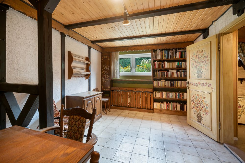 Heller Raum mit Holzmöbeln, Bücherregal, offenem Fenster und gemusterter Tür.
