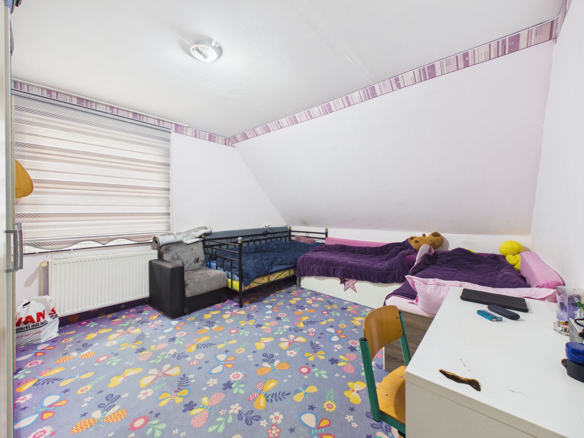 Helles Kinderzimmer mit zwei Betten, buntem Teppich, Schreibtisch und Dachschräge.