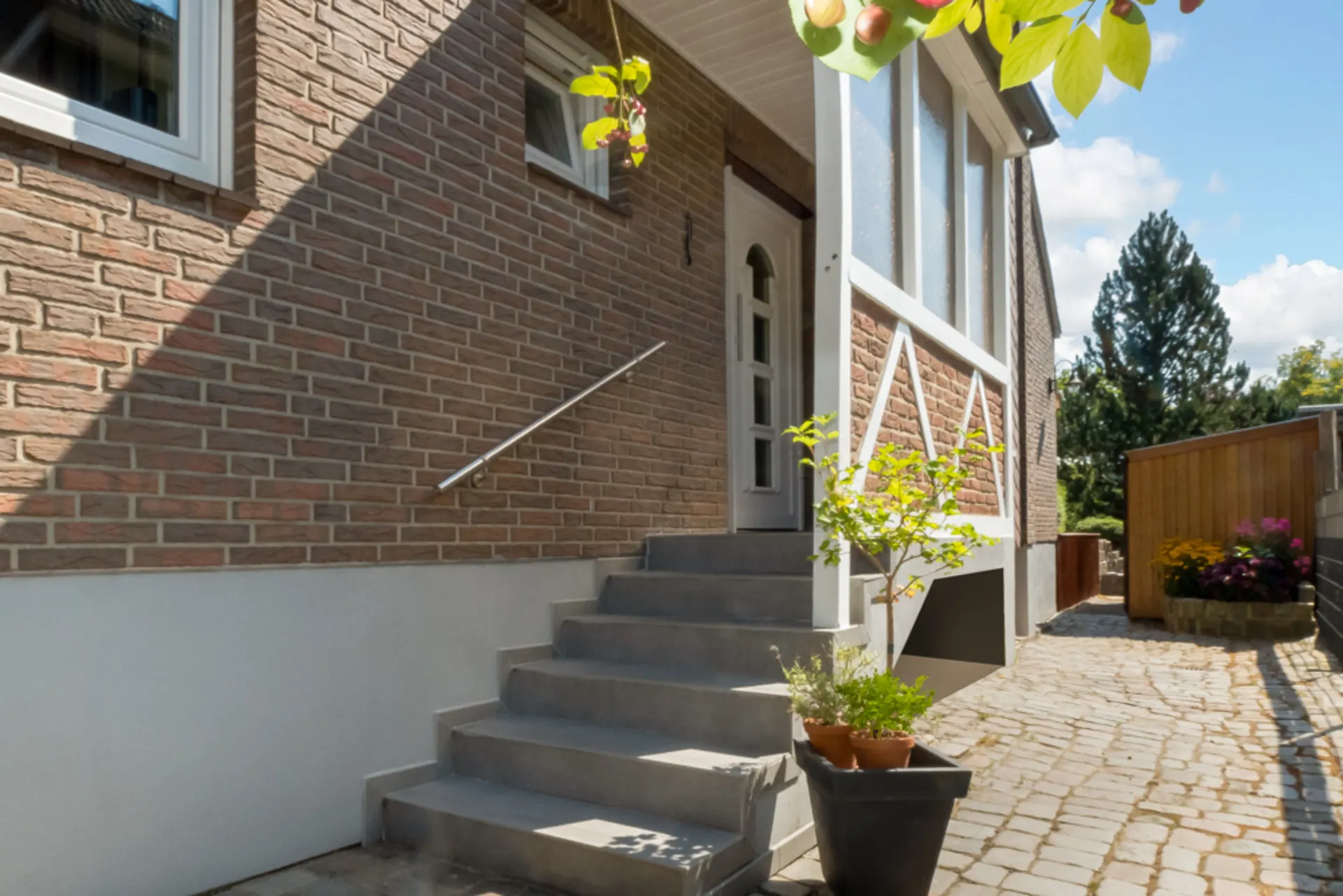 Eingangstreppe eines Backsteinhauses mit Pflanzen im Topf auf dem gepflasterten Weg.
