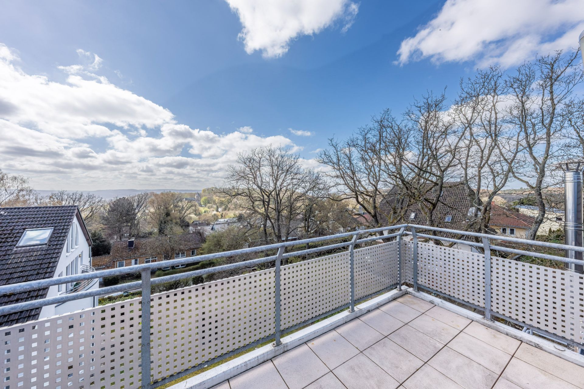 Blick von einem Balkon mit Metallgeländer auf Bäume und Nachbarhäuser bei Tageslicht.